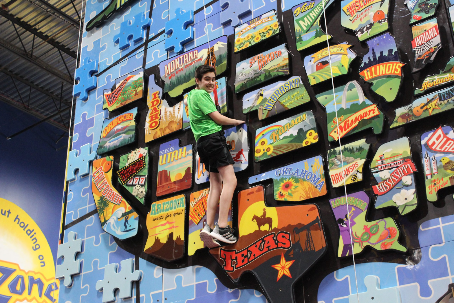 A boy in a green shirt climbing a wall shaped like a map of the United States at ClimbZone Laurel