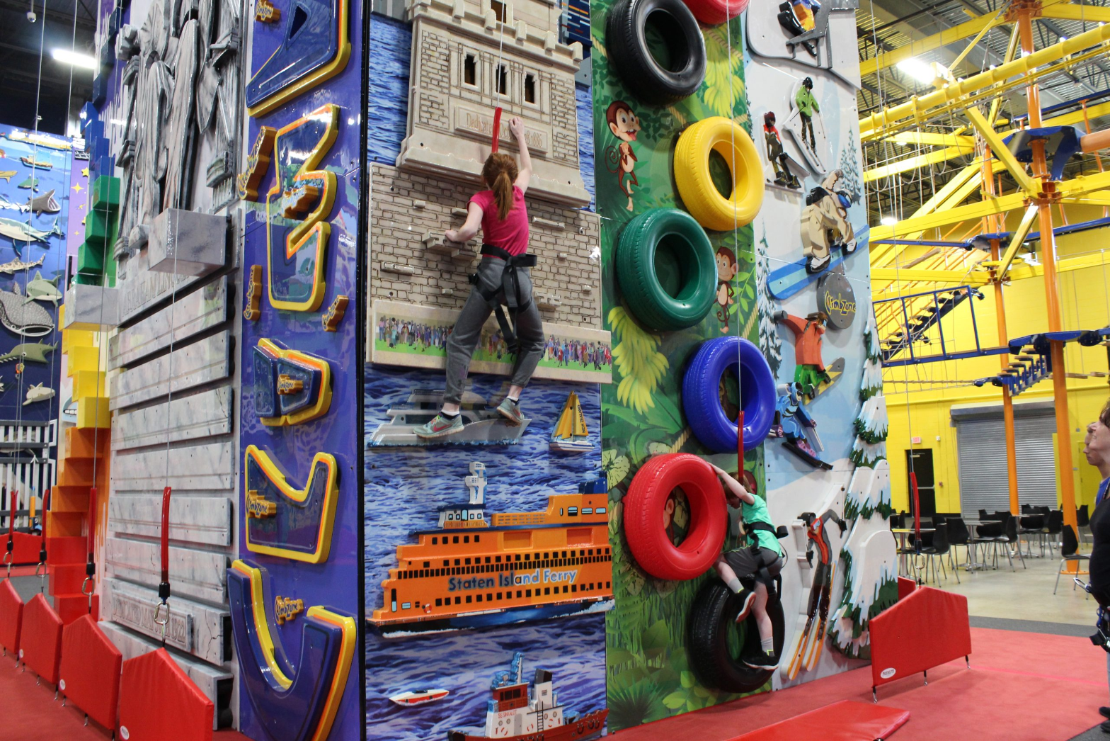 Themed climbing towers at ClimbZone Laurel, with a girl climbing the Statue of Liberty wall and a boy on the tyre wall